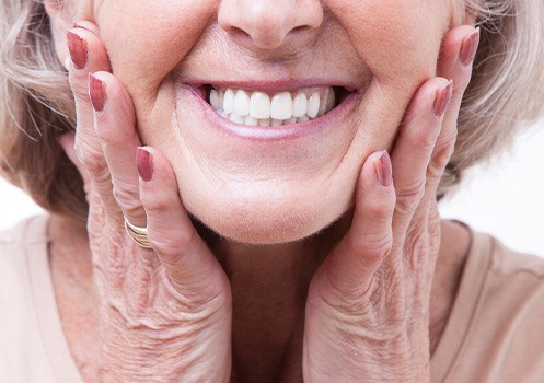 Nose-to-neck view of older woman smiling with hands pressed to cheeks