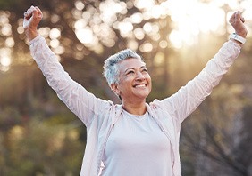 Woman outside near trees stretching arms up in victory