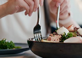 Hands holding forks scooping salad onto plate from bowl