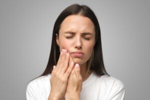 Woman touching one side of her jaw, grimacing in pain